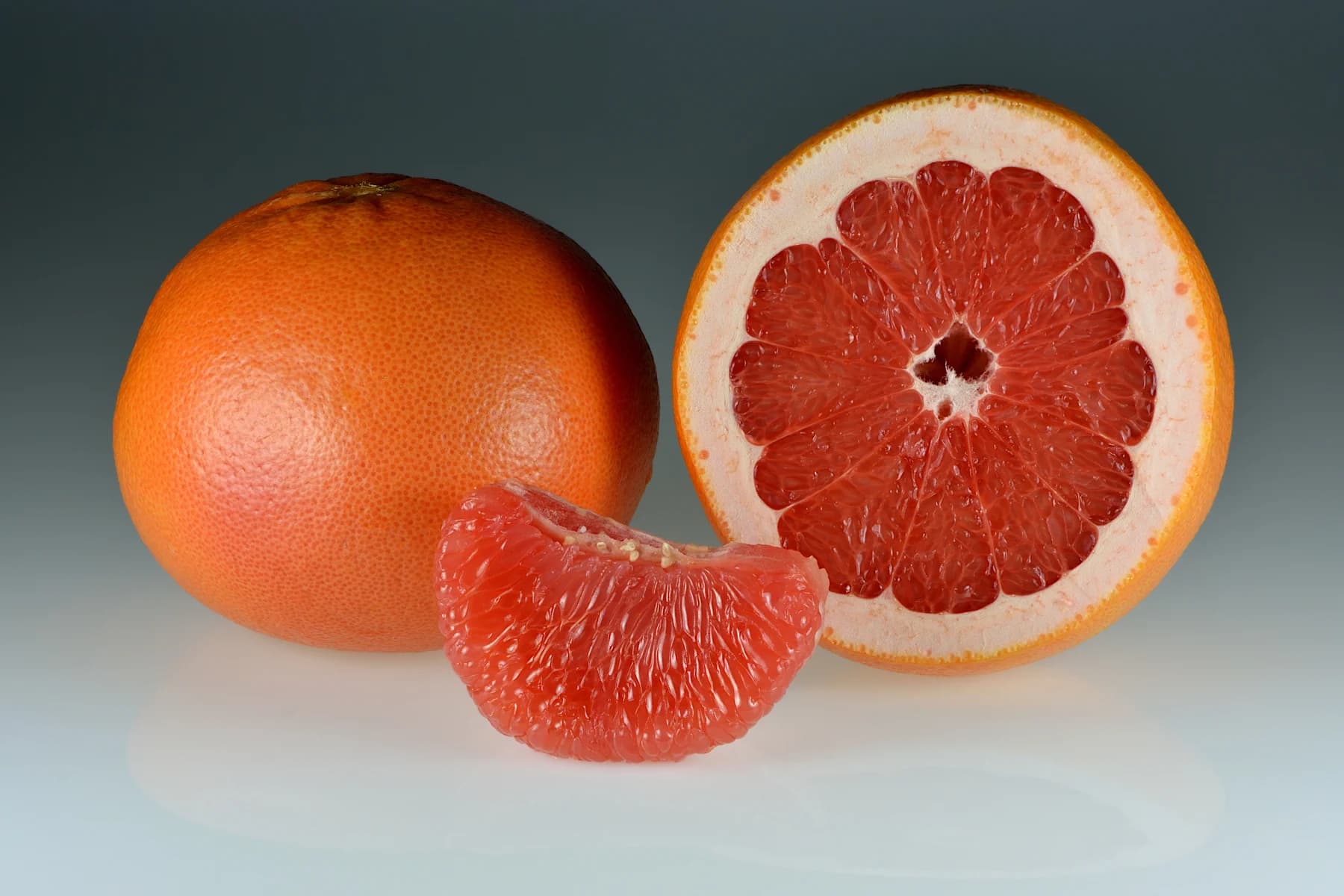 Whole red grapefruit, a cut half and a peeled segment
