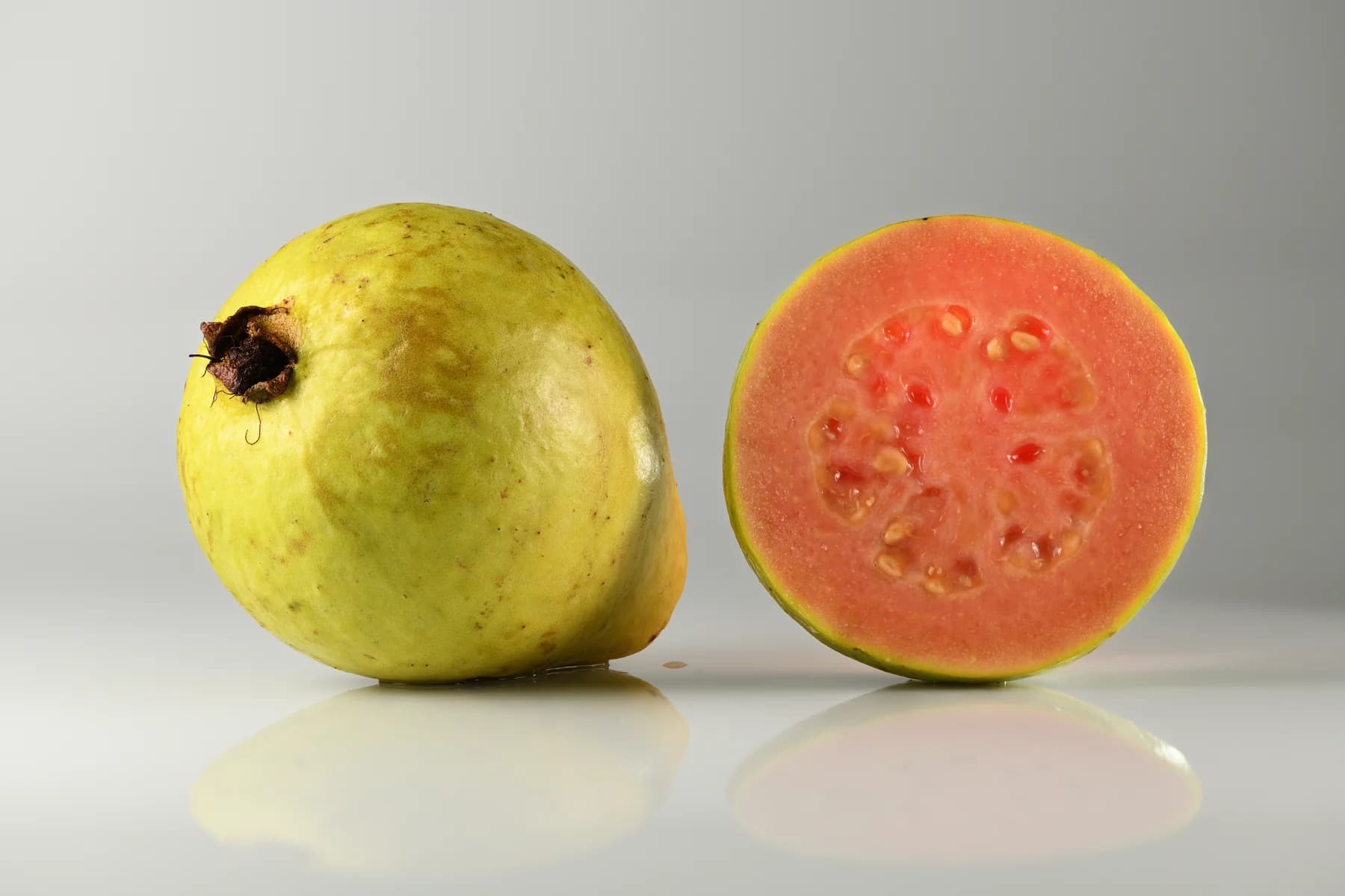 Whole guava and a cut half showing pink flesh and seeds