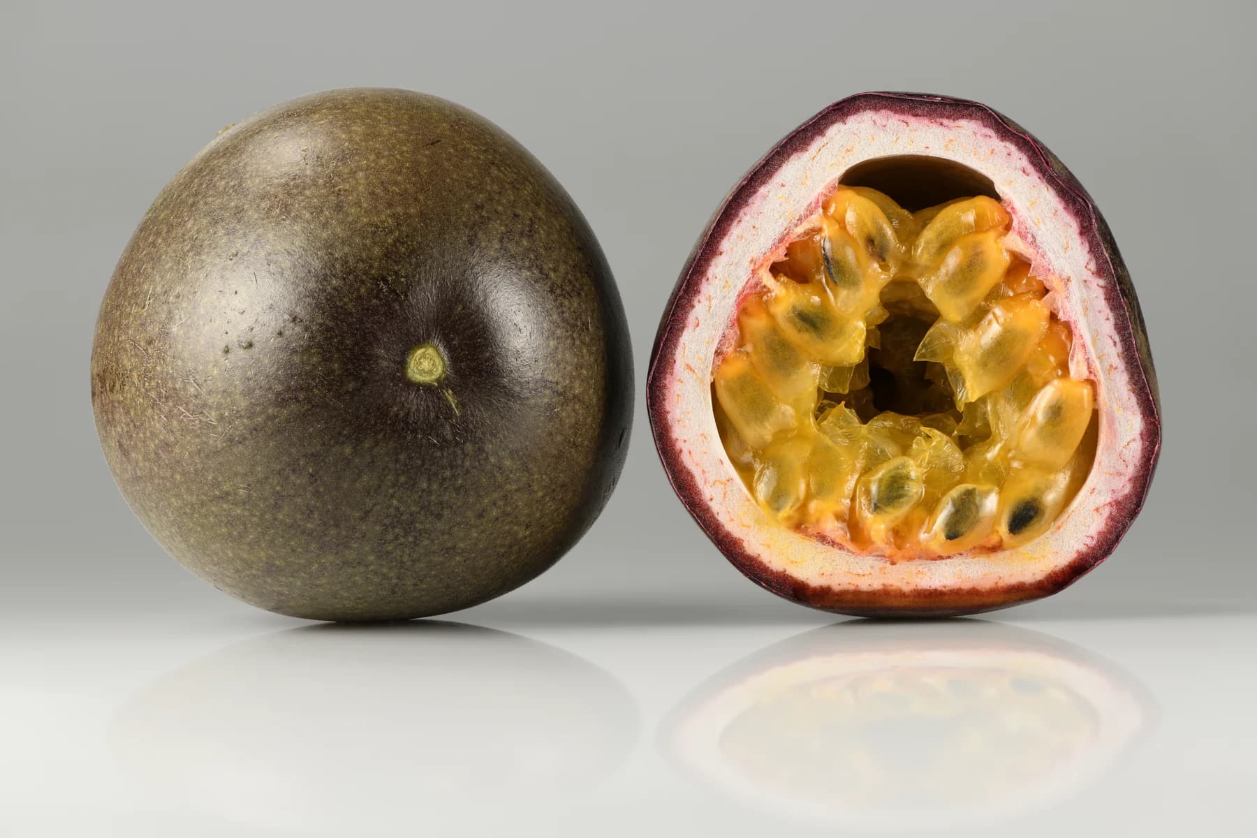 Whole purple passion fruit and a cut half showing pulp and seeds