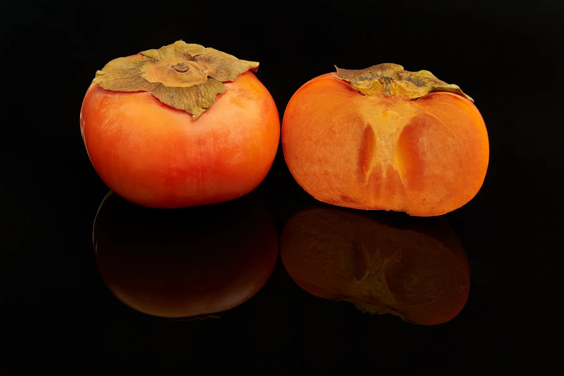 Whole Fuyu persimmon beside a cut half showing orange flesh