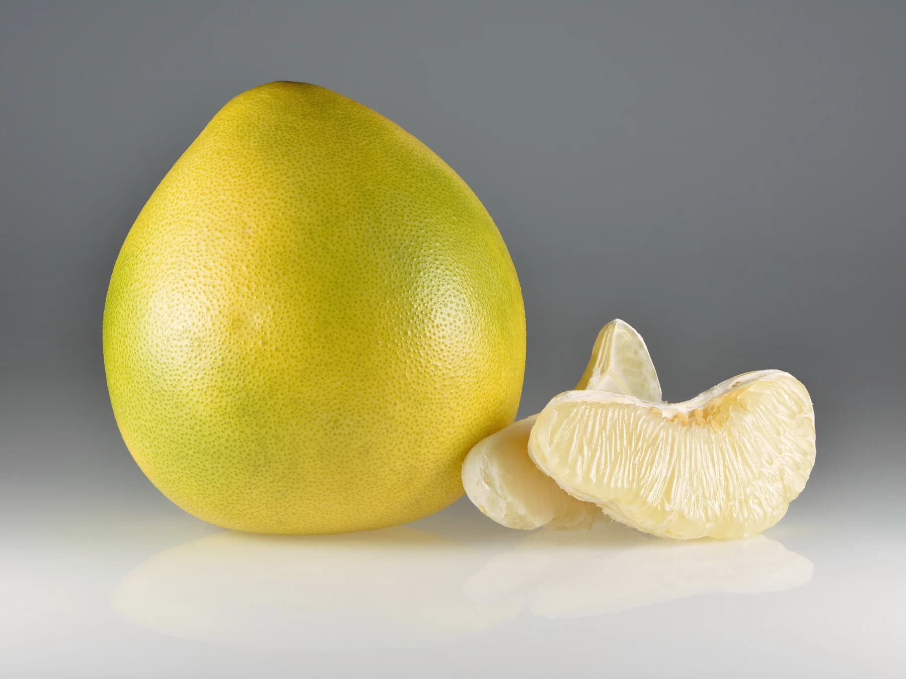 Whole yellow pomelo beside peeled pale-fleshed segments